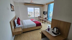A hotel room with a bed, a desk with a tray, a chair, a TV, and a window with a city view. - Park Niveda (Vijayawada)