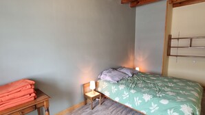 Un dormitorio con techo de madera, una cama con ropa de cama floral, una mesita de noche con una lámpara y una mesa con ropa doblada.
