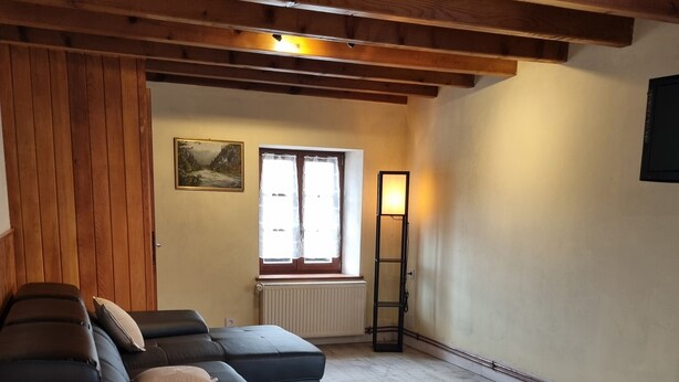 Una habitación con techo de madera, un sofá, un radiador, una ventana con cortinas y un cuadro en la pared.