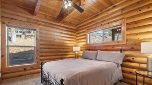 A log cabin bedroom with a bed, a window, a ceiling fan, and a nightstand. - Bear Creek Haven  (Big Bear Lake)