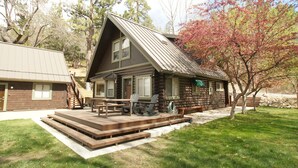 A log cabin with a deck, outdoor seating, and a stone wall in the background. - Bear Creek Haven  (Big Bear Lake)