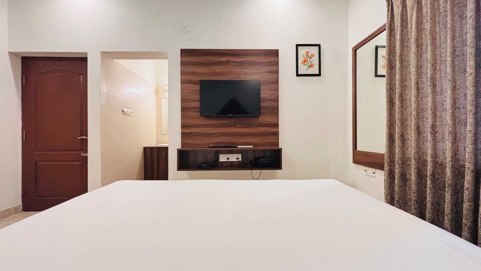 Een hotelkamer met een groot bed, een televisie bevestigd aan een houten paneel, een deur en een spiegel.