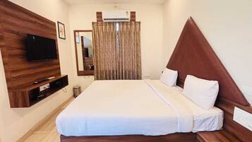 Quarto de hotel com uma cama grande, televisão de tela plana presa a um painel de madeira, um espelho e uma janela com cortinas.