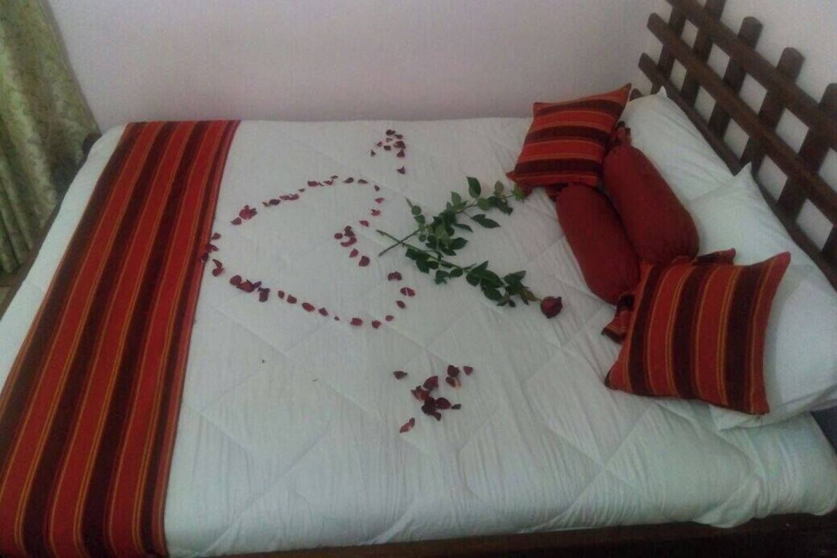 Una cama con colcha blanca, almohadas a rayas rojas y marrones, y un arreglo decorativo de hojas y flores sobre el edredón.