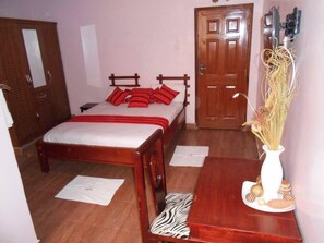 Een slaapkamer met een houten bed, een deur, een klein tafeltje met een vaas en een kussen met een zebraprint.