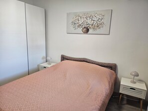 A bedroom with a bed, a nightstand, a lamp, a wardrobe, and a painting on the wall.