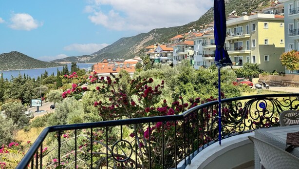 A balcony with a view of a coastal town, including buildings and a mountain in the background. - Moonlight Apart Sea View (Kas)
