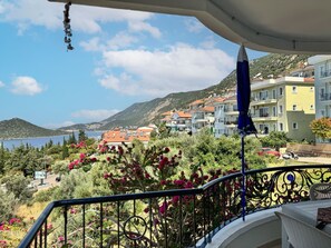 Un balcón con vistas a un pueblo costero, que incluye edificios y una montaña al fondo.