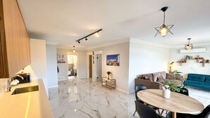 A modern kitchen with a marble countertop and a built-in sink. There is a dining area with a wooden table and black chairs. The living room features a blue sofa and a green couch. - Moonlight Apart Sea View (Kas)