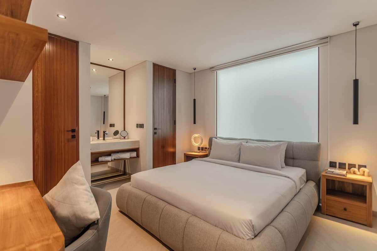 A modern bedroom with a large bed, a bedside table, a nightstand, a mirror, and a wardrobe.