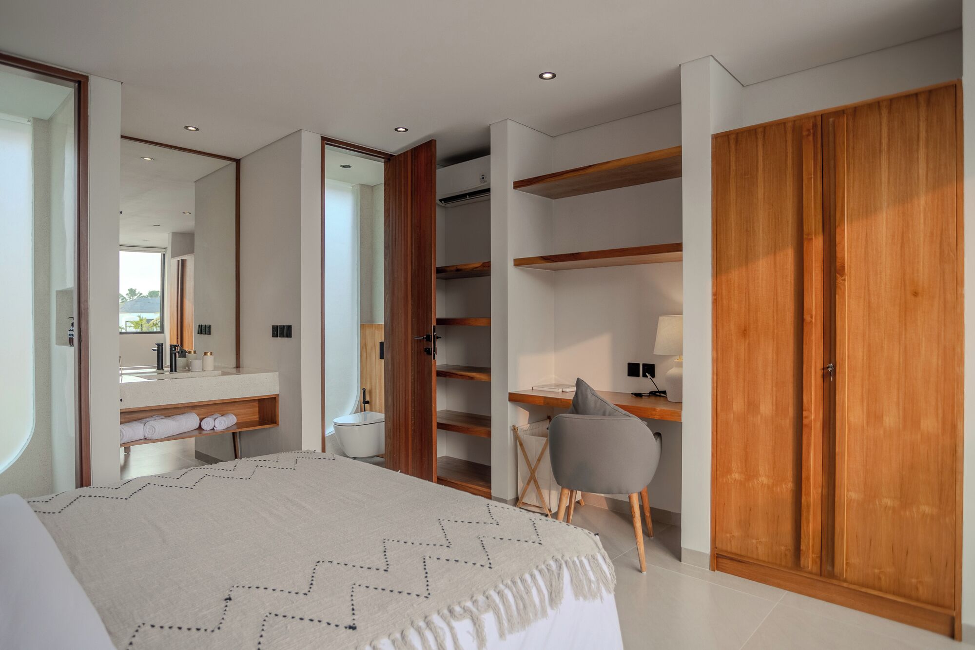 Un dormitorio con cama, escritorio, silla, armario y baño con espejo y lavabo.