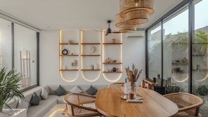 Een moderne eetruimte met een ronde houten tafel, rieten stoelen en een hangende geweven lamp.