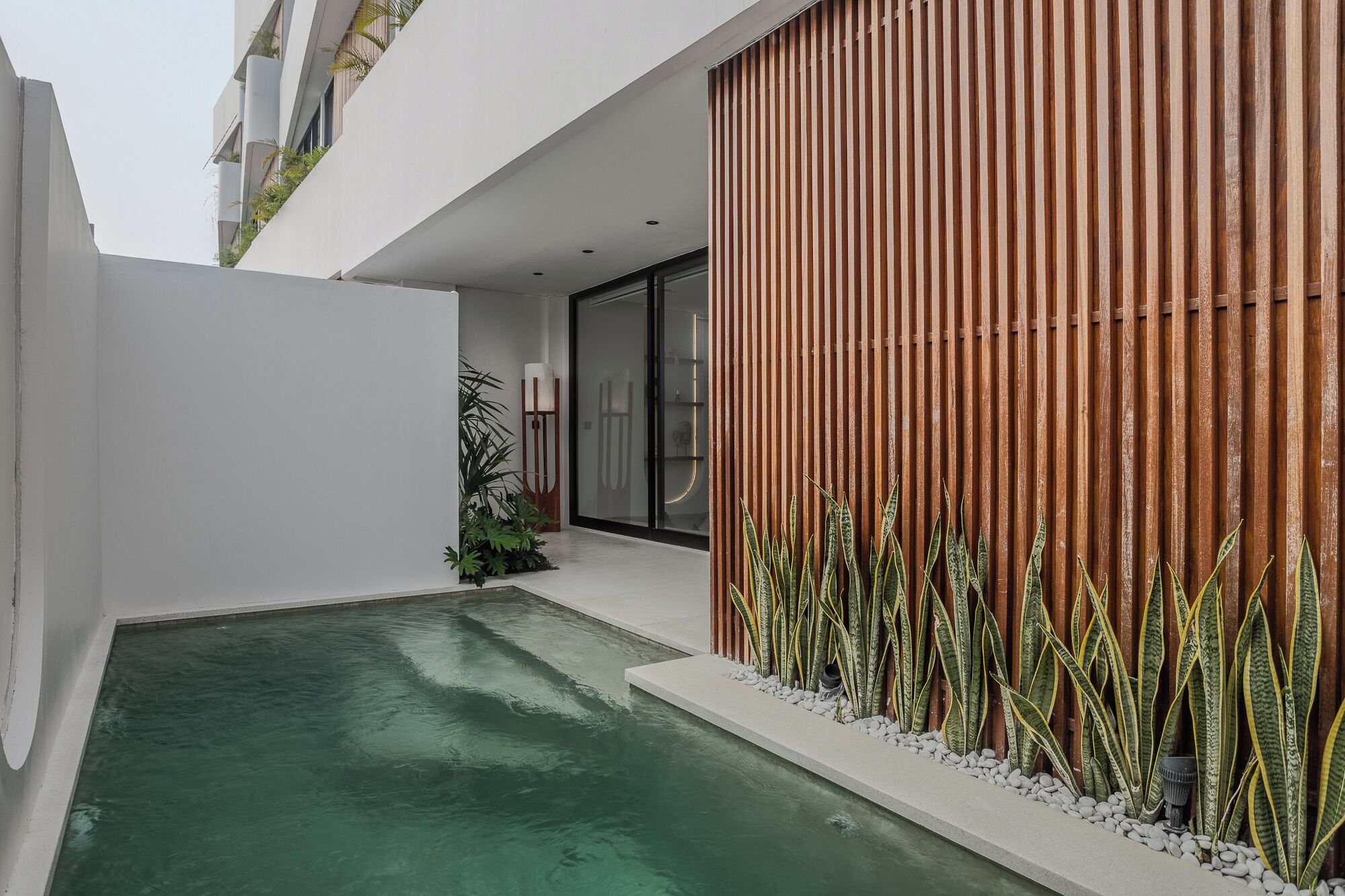 A modern building with a pool, a wooden slatted wall, and potted plants.