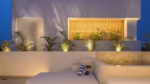 Een moderne, open loungeruimte met een minimalistisch design, met een grote witte bank, een klein tafeltje en een houten lambrisering met planten.