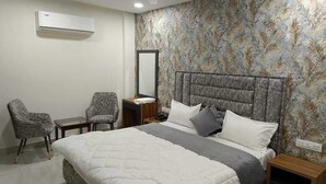 Een slaapkamer met een bed, twee fauteuils, een nachtkastje, een spiegel en een airconditioning.