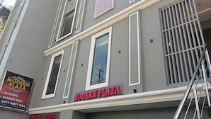 A building with a sign reading "MODERN PLAZA" and another sign listing amenities like "AL ROOMS," "BANQUET HALL," and "KITTY PARTY HALL."