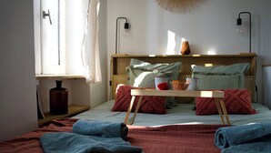 A room with a bed, a wooden headboard, a bedside table, a window with curtains, and a wall-mounted light fixture.
