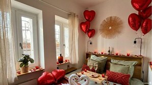 A cozy room with a bed, a bedside table with candles, and heart-shaped balloons.