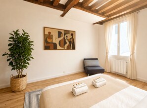 A hotel room with a bed, a potted plant, a painting, and a window with curtains.