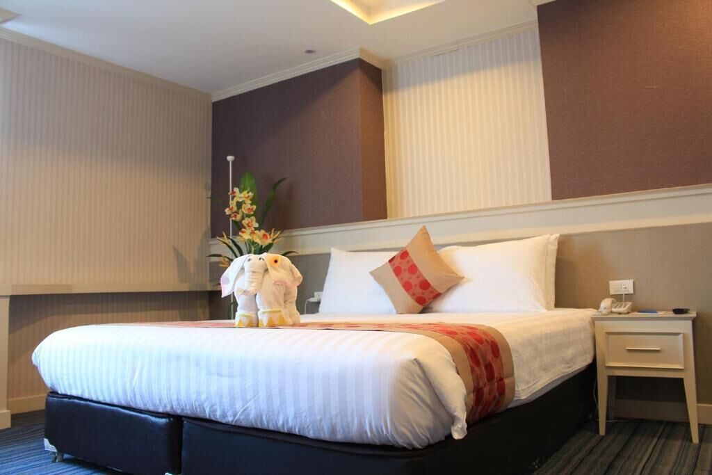 A hotel room with a large bed, a nightstand, a telephone, and a decorative plant.