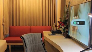 A hotel room with a red sofa, a grey armchair, a desk with a flat-screen TV, and a wooden floor. - Vwish Hotel Khon Kaen (Khon Kaen)