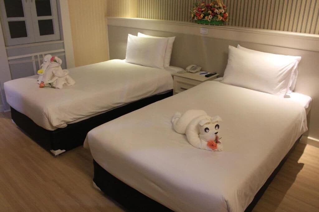 Two adjacent hotel beds with white linens, a bedside table with a phone, and a decorative floral arrangement on the wall.