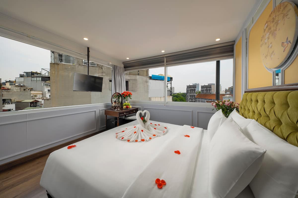 A hotel room with a large bed, a television on the wall, and a view of the city through the window.