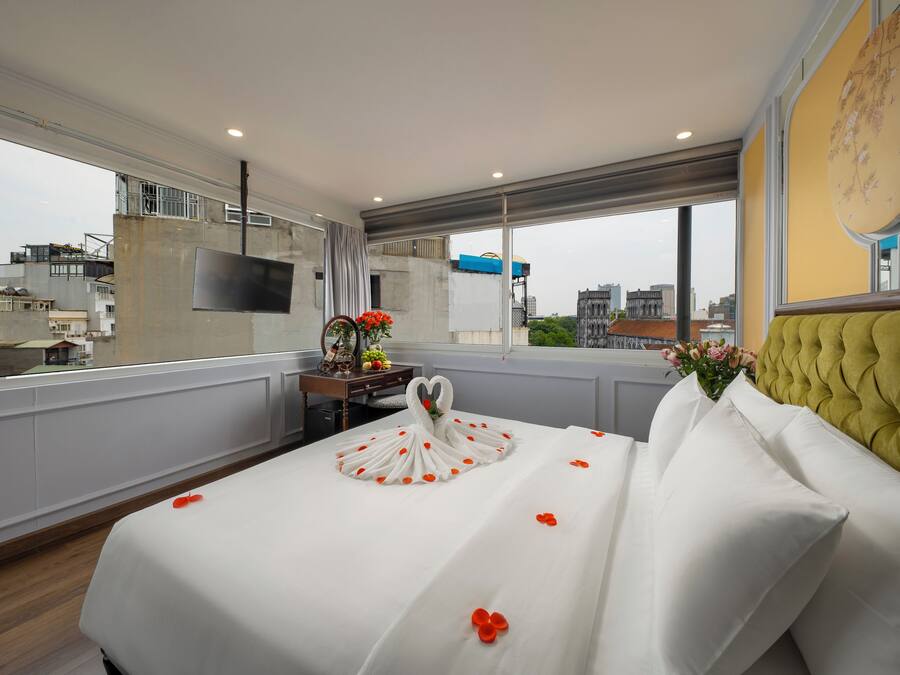 A hotel room with a large bed, a television on the wall, and a view of the city through the window.