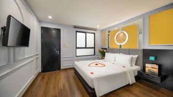 Una habitación de hotel con cama, televisión, mesita de noche, espejo y ventana.