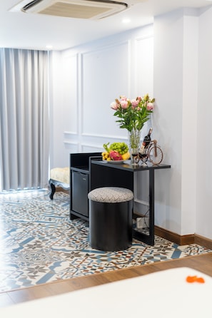 A hotel room with a bed, a desk with a vase of flowers, a bicycle, and a minibar. - Hanoi Royal Premium Hotel (Hanoi)