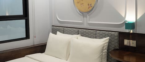 A hotel room with a bed, a decorative wall hanging, a patterned headboard, and a bedside table with a lamp.