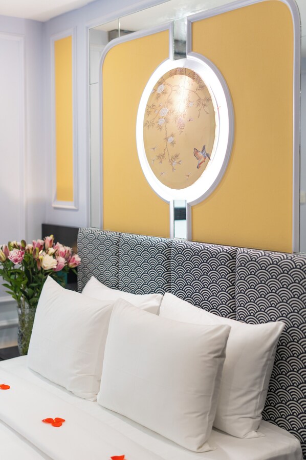Un lit avec une literie blanche et des pétales de fleurs rouges, un miroir rond orné de motifs floraux et une tête de lit à motifs.