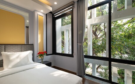 A hotel room with a large window, a bed, a nightstand, and a vase with flowers.
