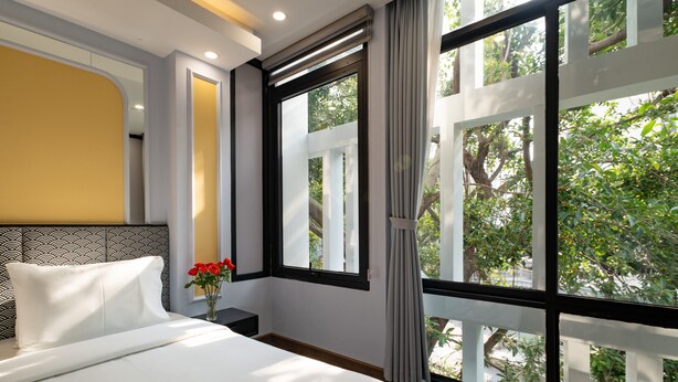 Une chambre d’hôtel avec une grande fenêtre, un lit, une table de chevet et un vase rempli de fleurs.