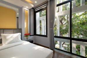 Une chambre d’hôtel avec une grande fenêtre, un lit, une table de chevet et un vase rempli de fleurs.