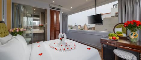 Habitación de hotel con cama, escritorio, silla, televisor y vista a la ciudad.