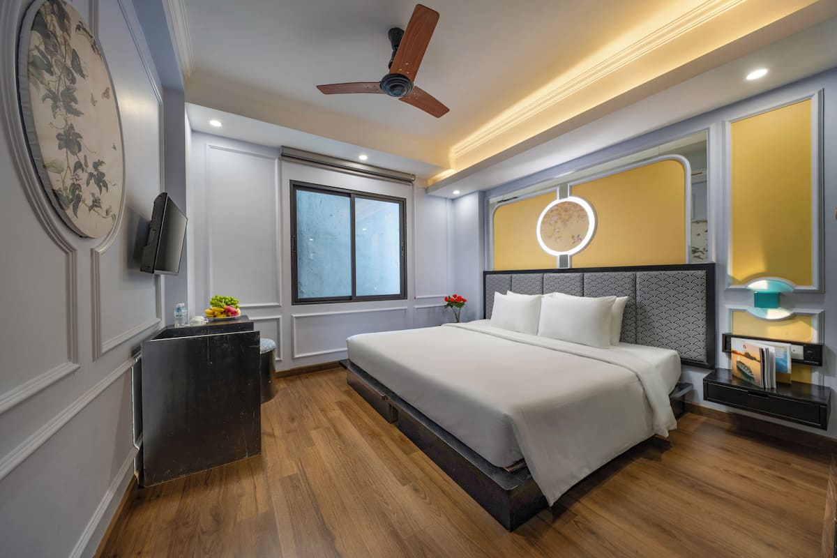 A modern bedroom with a bed, a ceiling fan, a TV, a bedside table, a nightstand, and a window.