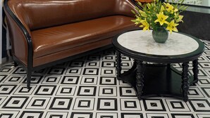 Une pièce avec un canapé en cuir marron, une table ronde ornée d’un vase de fleurs jaunes et un grand tableau abstrait accroché au mur.