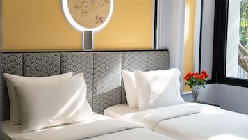 A hotel room with a bed, pillows, a round mirror, and a vase with flowers.
