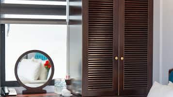 A hotel room with a large bed, a wooden wardrobe, a round mirror, a bedside table with a phone, and a window with blinds.