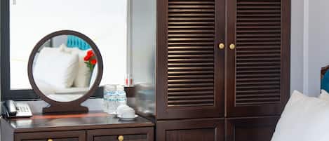 A hotel room with a large bed, a wooden wardrobe, a round mirror, a bedside table with a phone, and a window with blinds.