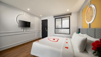 A hotel room with a bed, a TV mounted on the wall, a window, and a clock on the wall.