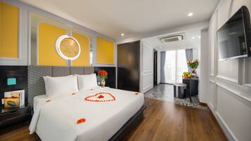 A hotel room with a large bed, a bedside table with a lamp, a mirror, and a TV on the wall.