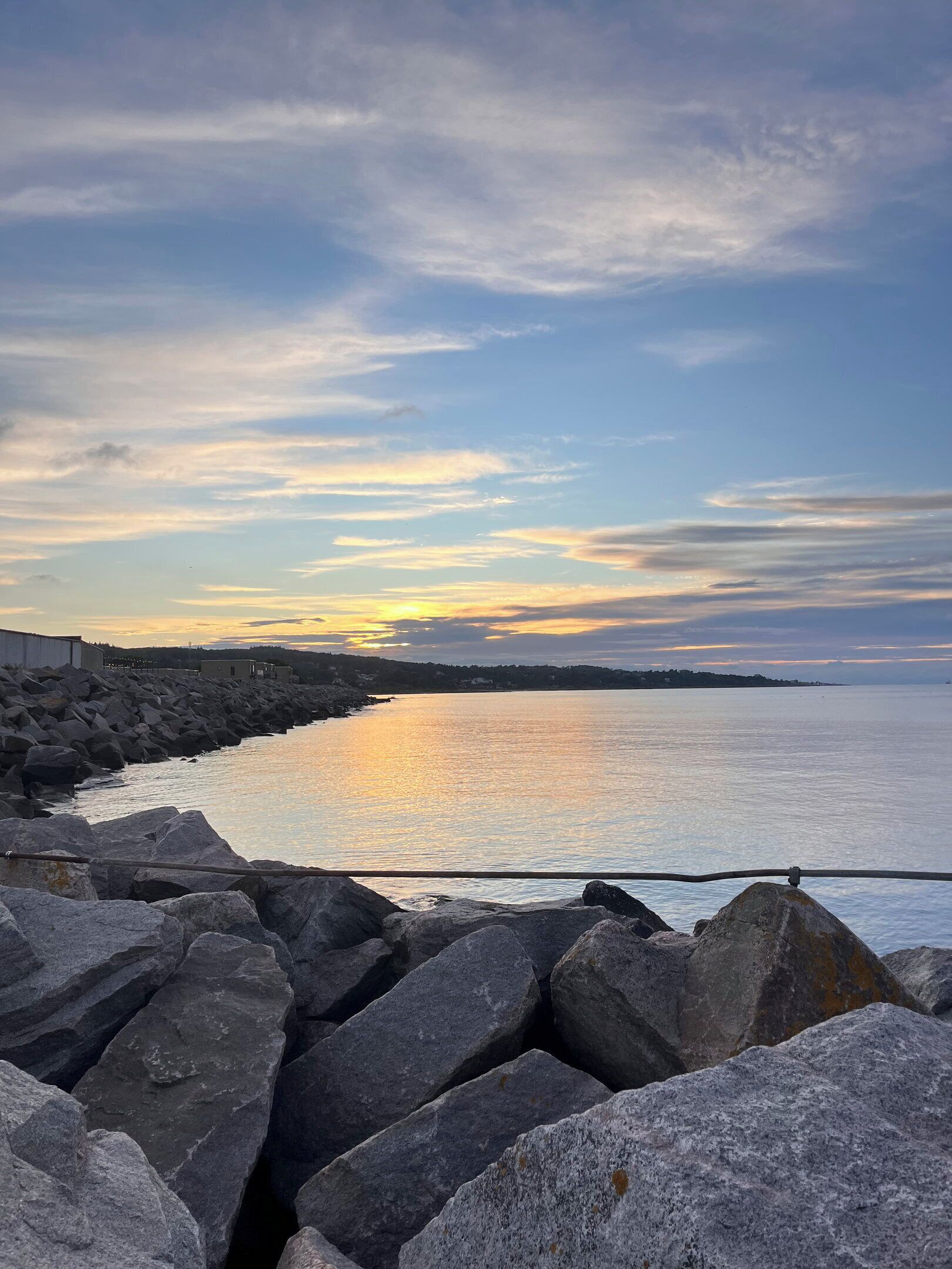 A coastal landscape with a rocky shoreline, a calm sea, and a sunset.