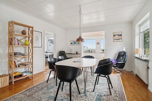 Una habitación amplia con una mesa redonda, sillas negras, una estantería de madera y una alfombra estampada.
