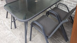 A patio area with a glass-top table and four chairs, a brick wall, and a metal gate. - Immaculate Entire House in Chermside West 2-Beds (Chermside West)