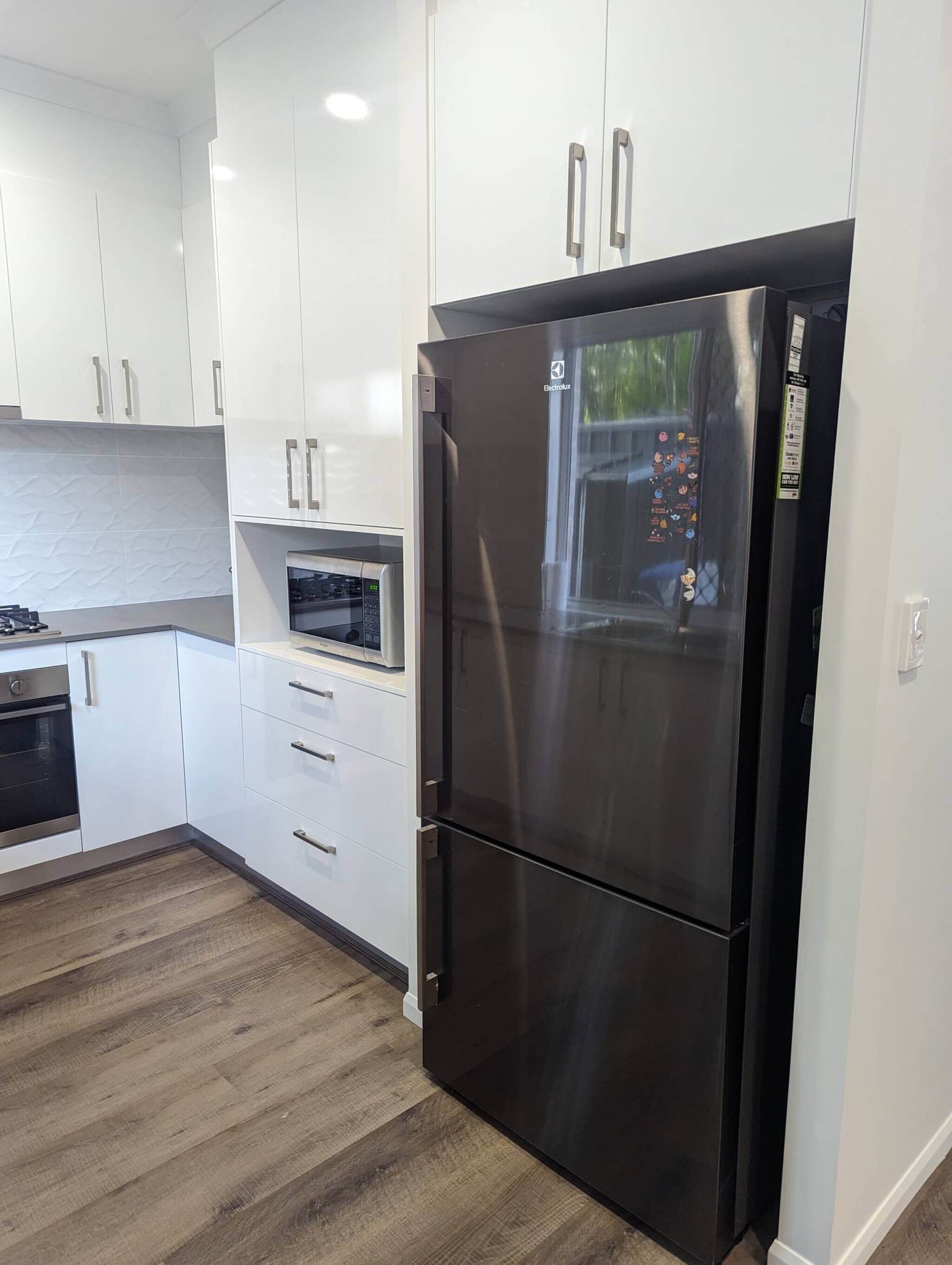 Una cocina moderna con armarios blancos, un refrigerador de acero inoxidable, un microondas y un horno empotrado.