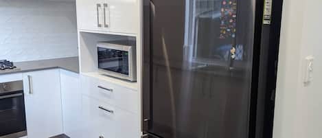 Una cocina moderna con armarios blancos, un refrigerador de acero inoxidable, un microondas y un horno empotrado.