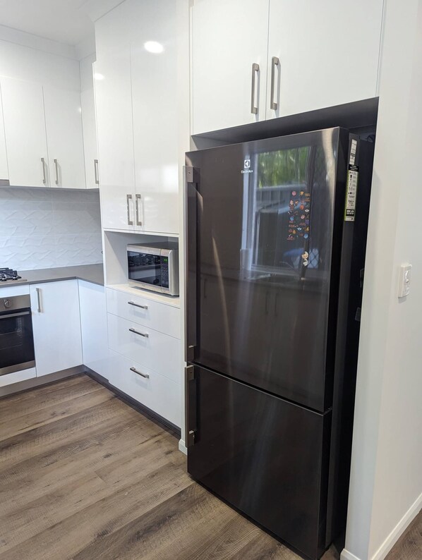 A modern kitchen with white cabinets, a stainless steel refrigerator, a microwave, and a built-in oven.