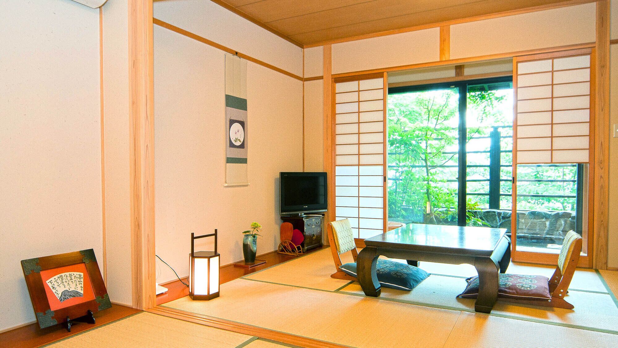 Une pièce de style japonais traditionnel, avec un sol recouvert de tatamis, une table basse, un téléviseur et une porte coulissante donnant sur un paysage verdoyant.